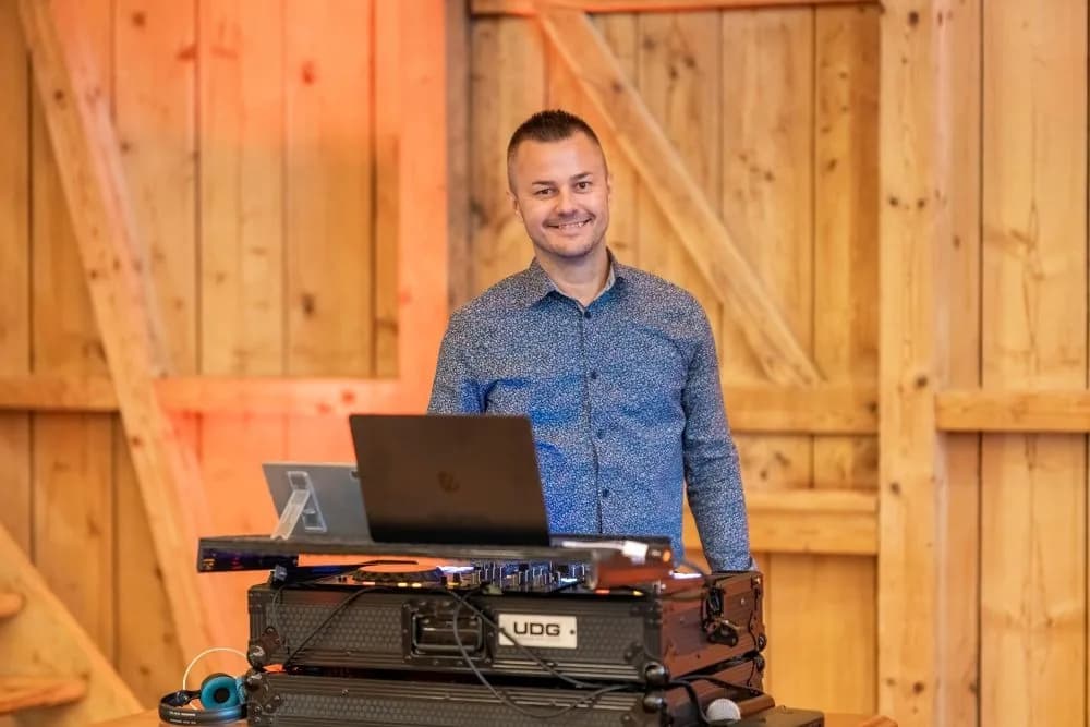 DJ Canis hinter seinem aufgebauten Mischpult in einem Holzsaal