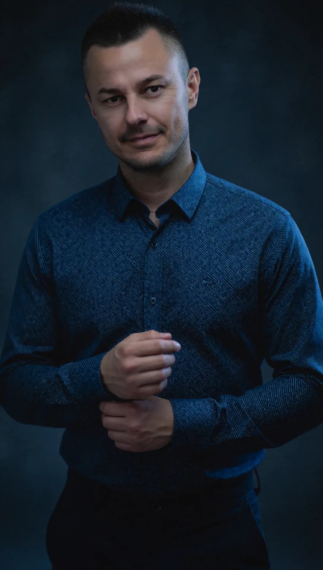 DJ Canis im blauen Hemd vor dunklem Hintergrund